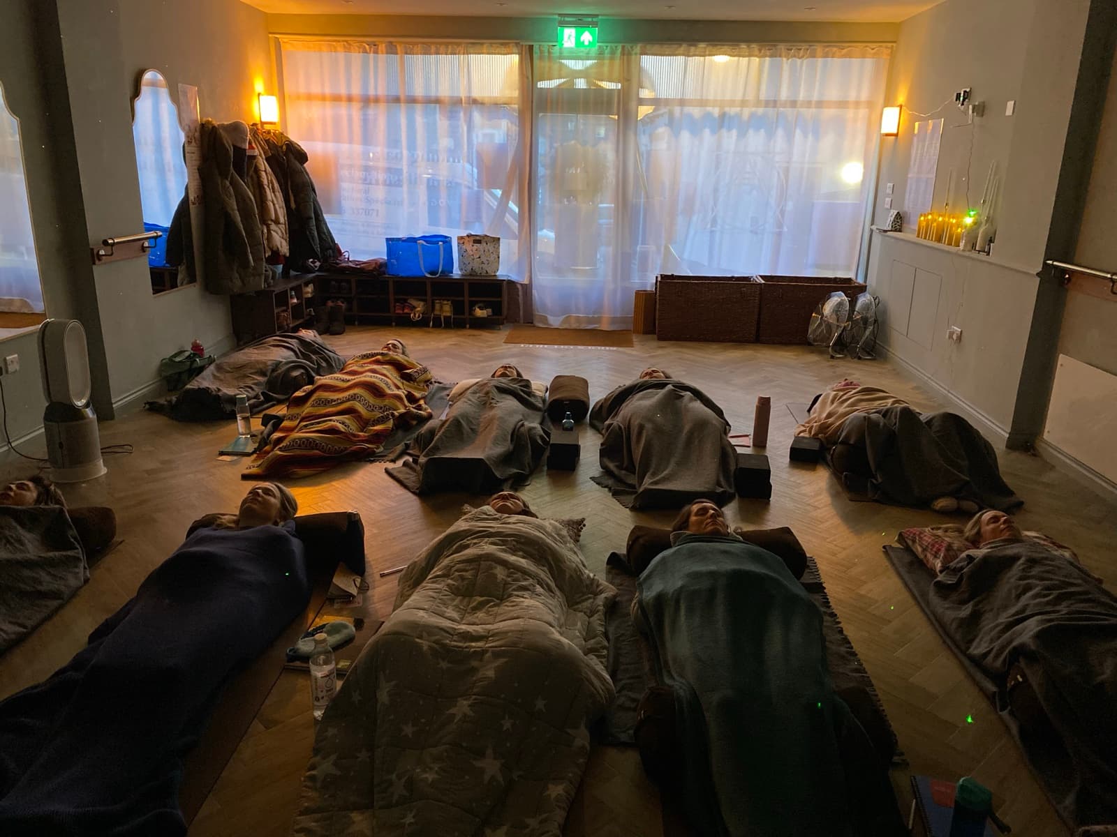 A yoga nidra class lying still under blankets and bolsters on the floor of a candlelit hall, resting in savasana — group yoga nidra in North Essex