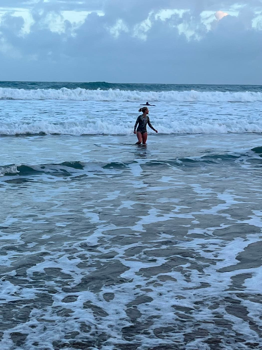 Candace standing waist deep in breaking surf at first light, cold water swimming off a wide sandy beach